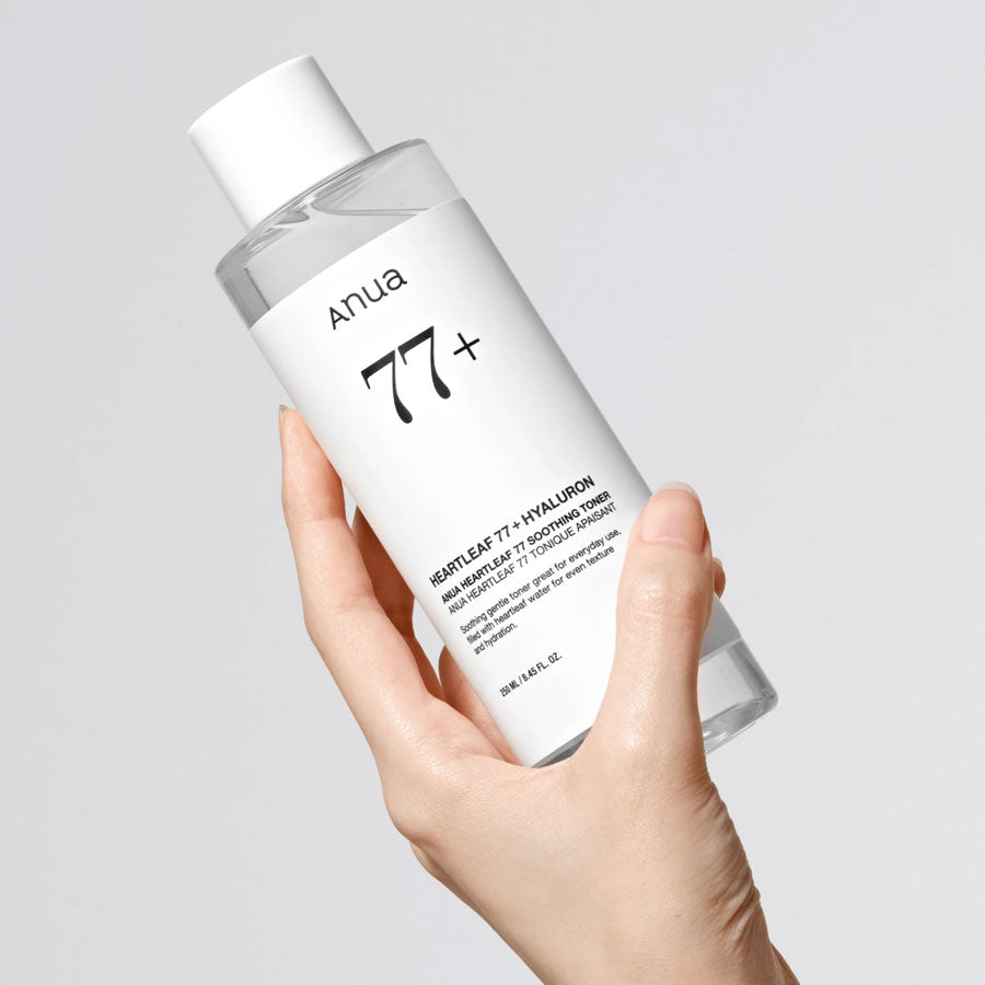 Hand holding a bottle of Anua 77+ skincare product on a light gray background